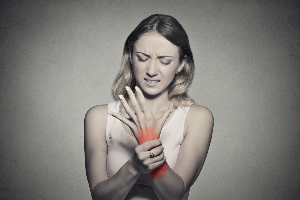 The woman experiences wrist joint pain, gripping her wrist with discomfort.