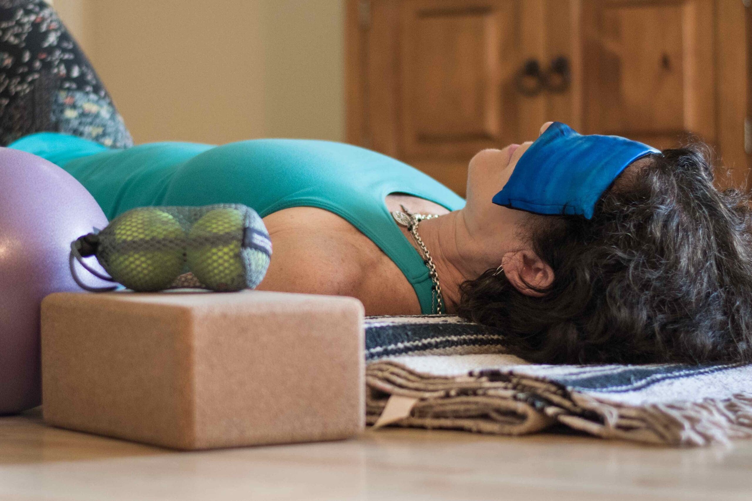 A woman is positioned on a yoga mat on the floor, accompanied by a ball, representing a serene exercise environment.